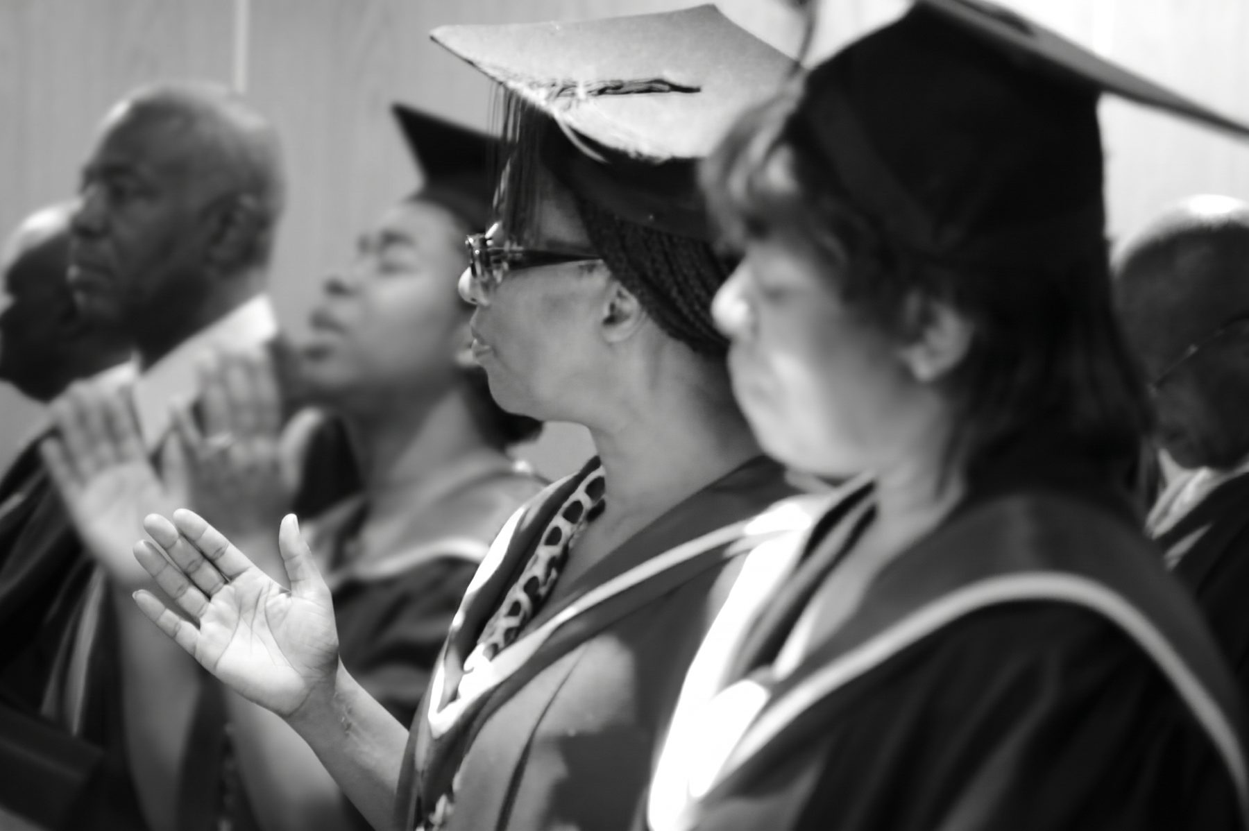BIBS graduates in caps and gowns, hands raised in prayer and worship at a graduation service